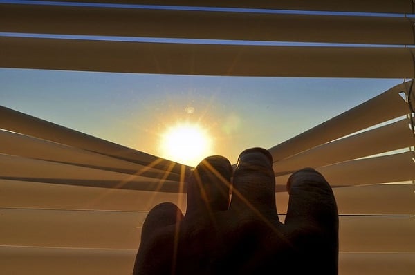 beobachten, wie die Sonne durch die heruntergelassene Lamelle eines Fensterladens hervorlugt